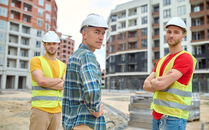 Reliability. Engineer and two workers in protective helmet standing confidently looking at camera at construction site during day